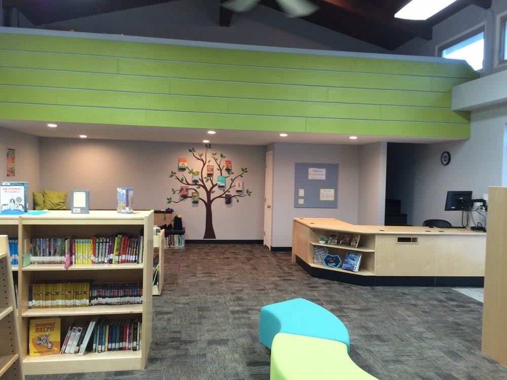 Library interior with bookshelves, a service desk, and a tree mural