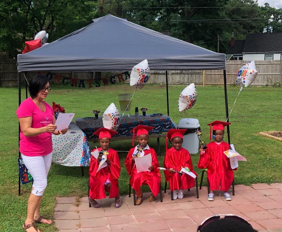 Person speaking to four children in graduation caps and gowns