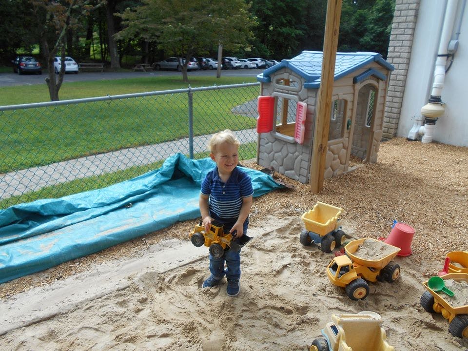 Child standing in a sandbox holding a toy truck