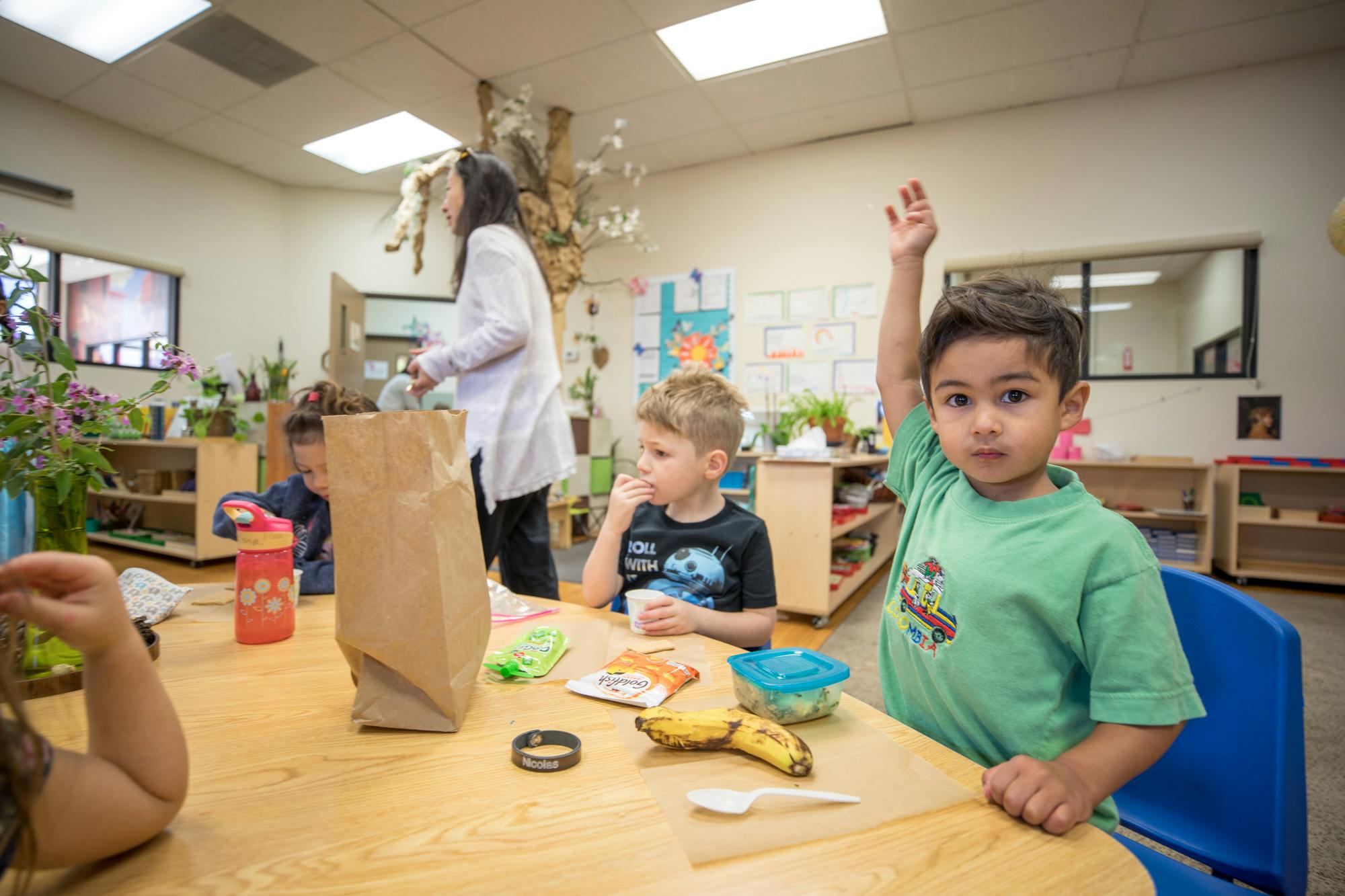 Child raising hand at a table in a classroom