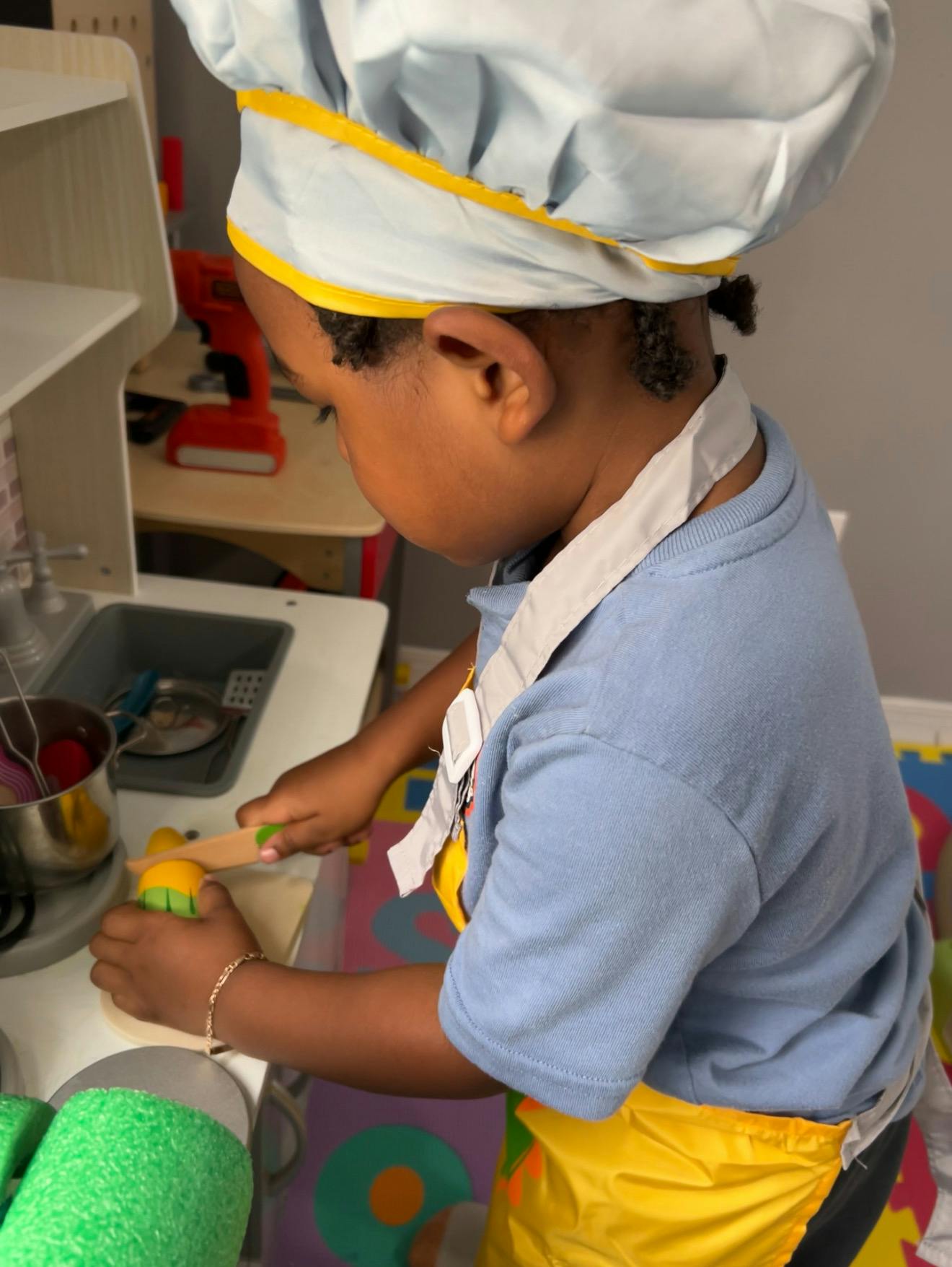 Child wearing a chef hat and apron playing with a toy kitchen