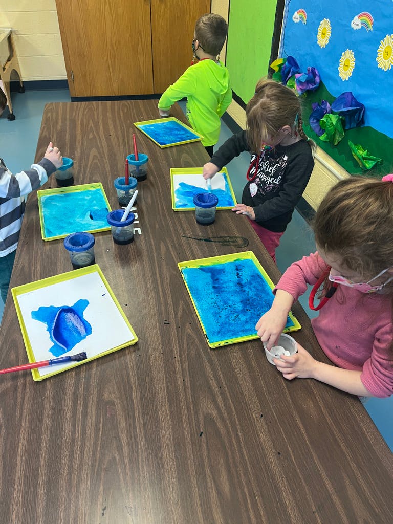 Children painting at a table in a classroom
