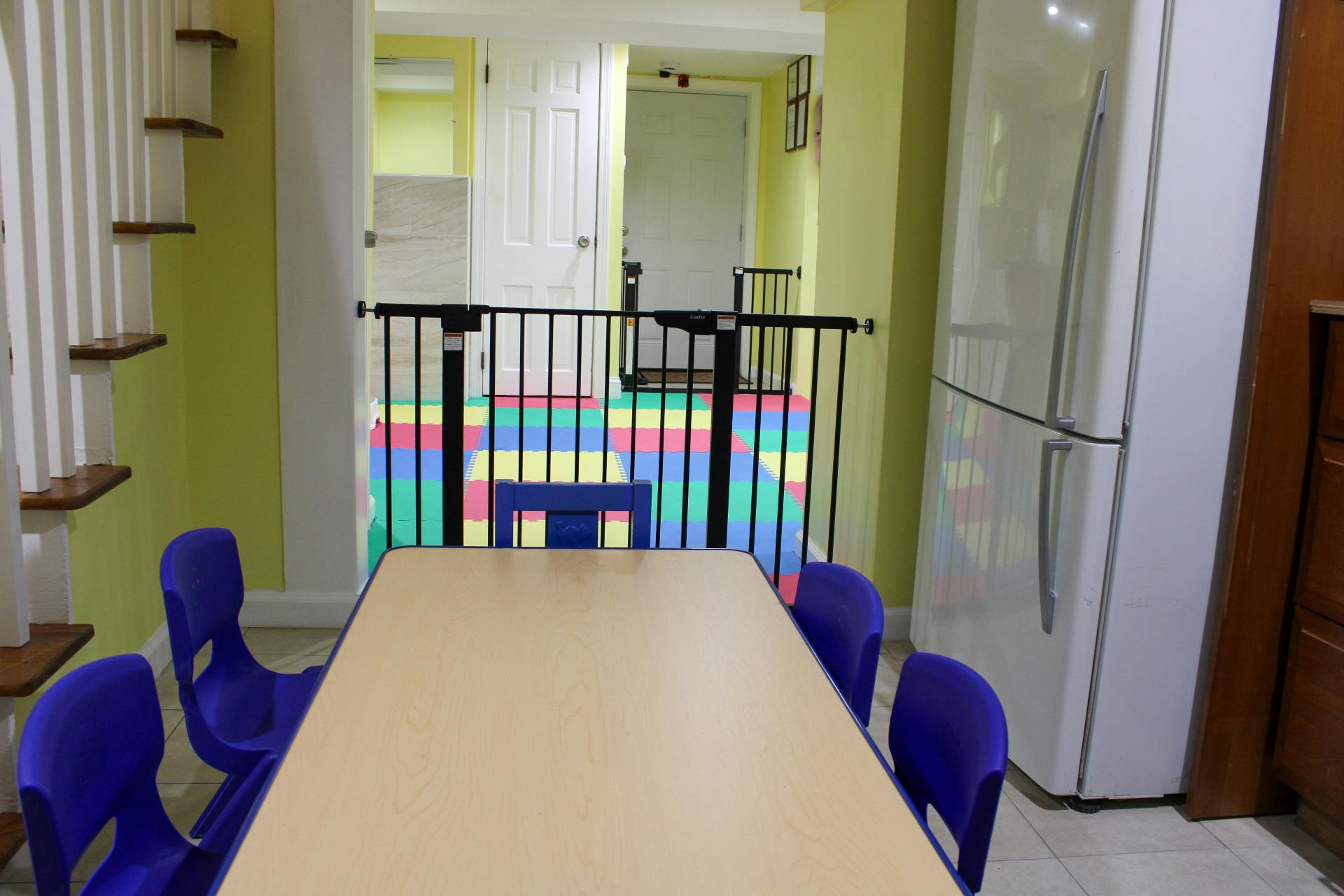 Table with purple chairs in a room with a play area and refrigerator