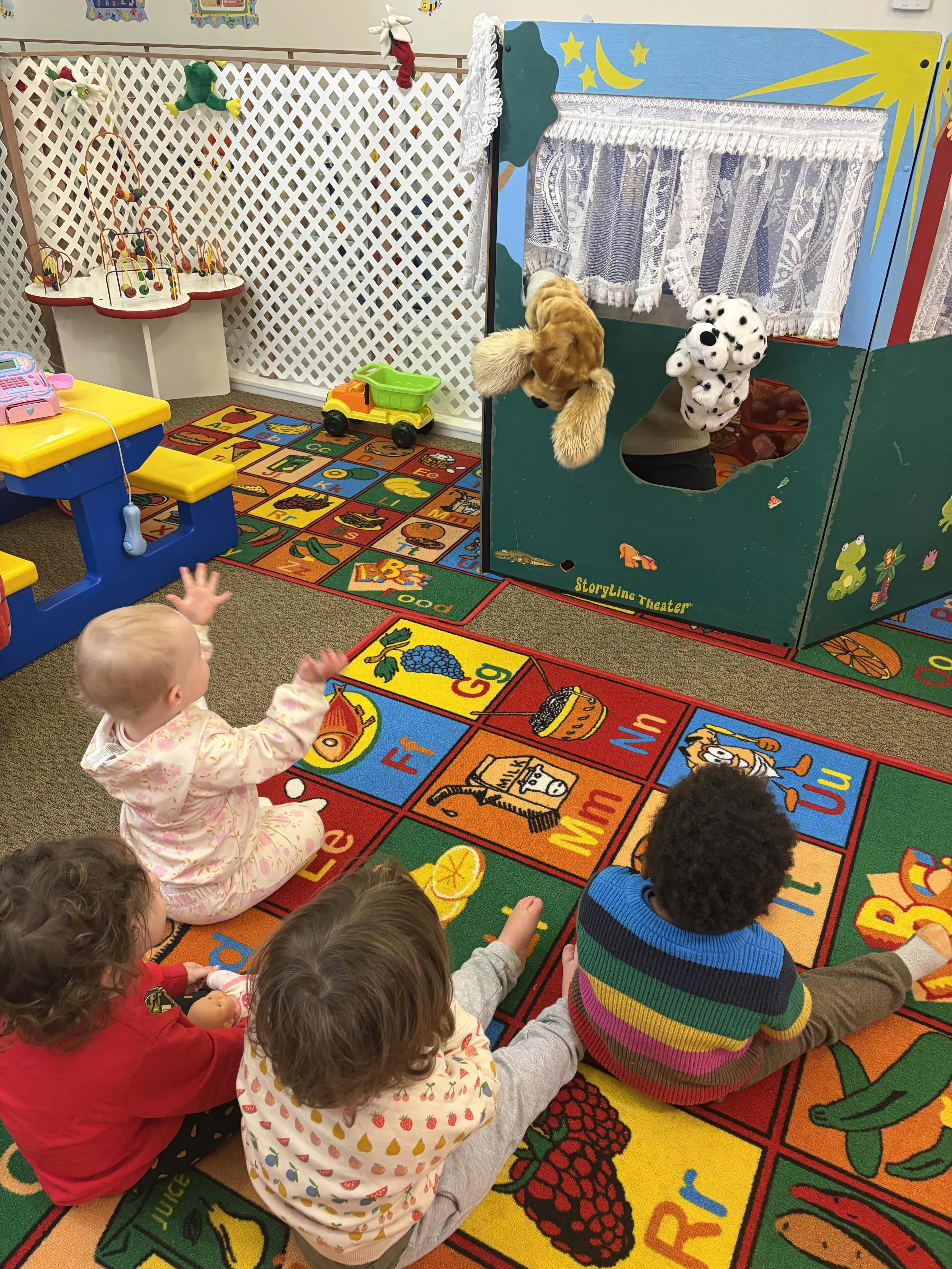 Children sitting on a rug watching a puppet show in a classroom