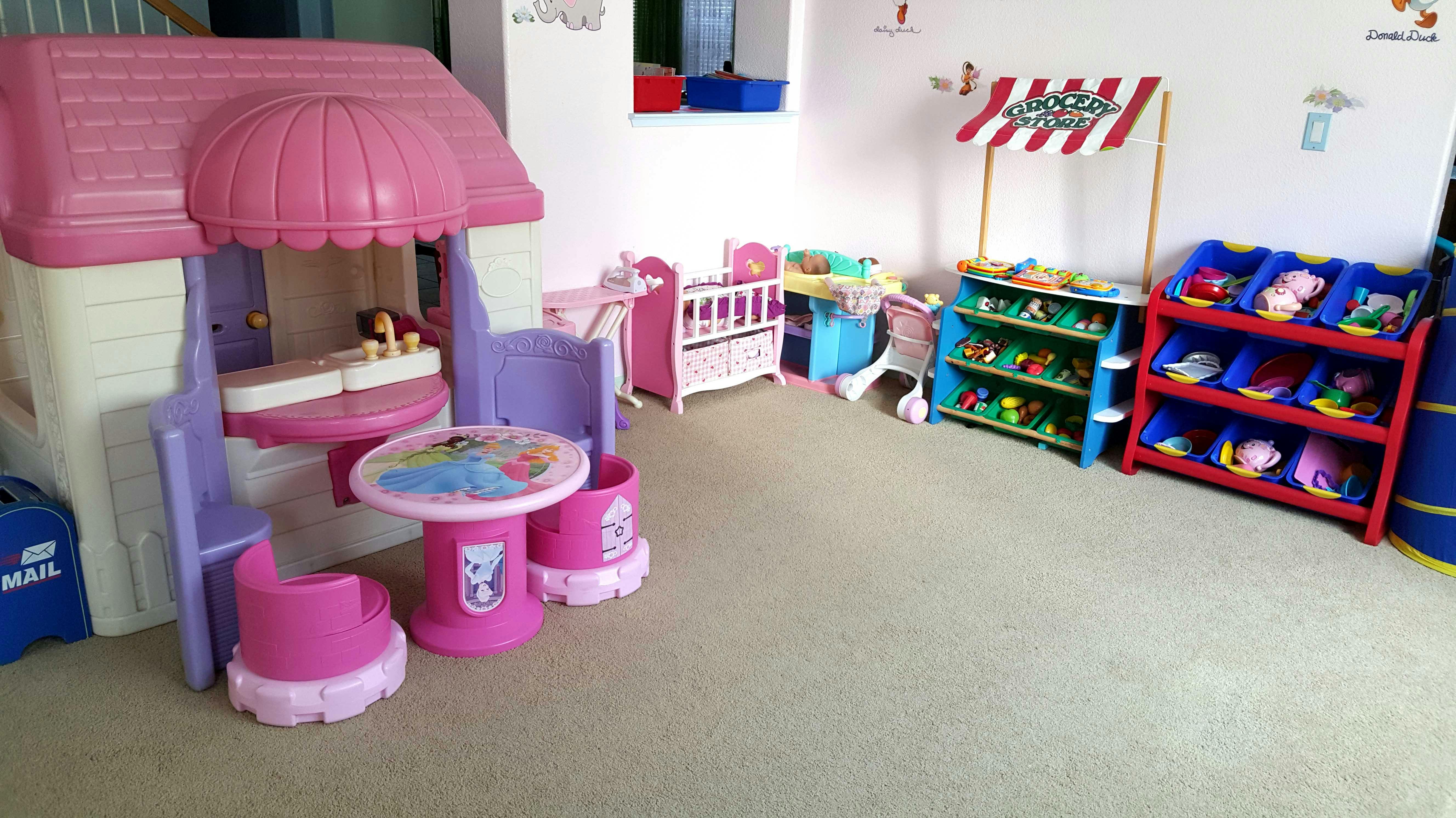 Playroom with toy house, table and chairs, and shelves with shelves of toys