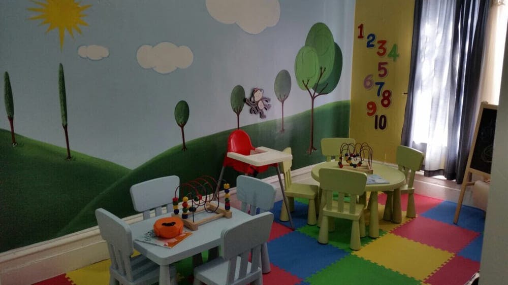 Playroom with small tables and chairs, colorful floor mats, and wall mural