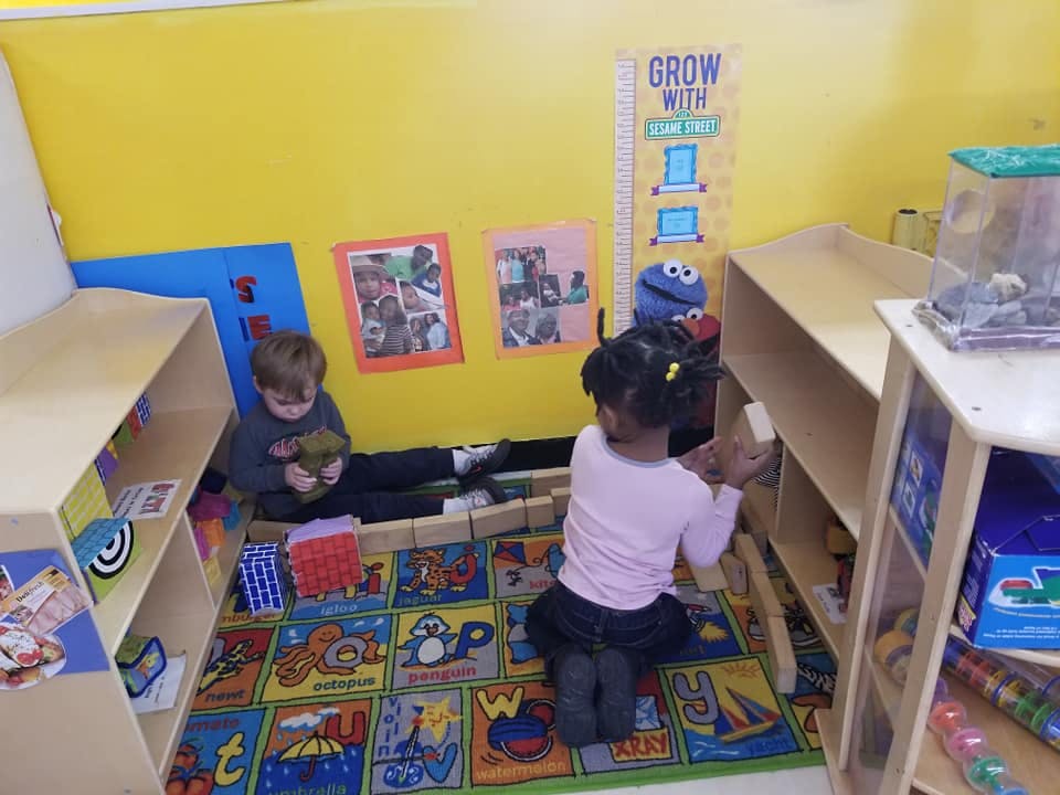 Two children playing on a colorful rug in a classroom