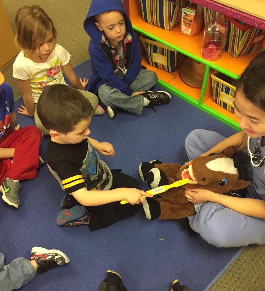 Child brushing teeth of a stuffed horse with an adult