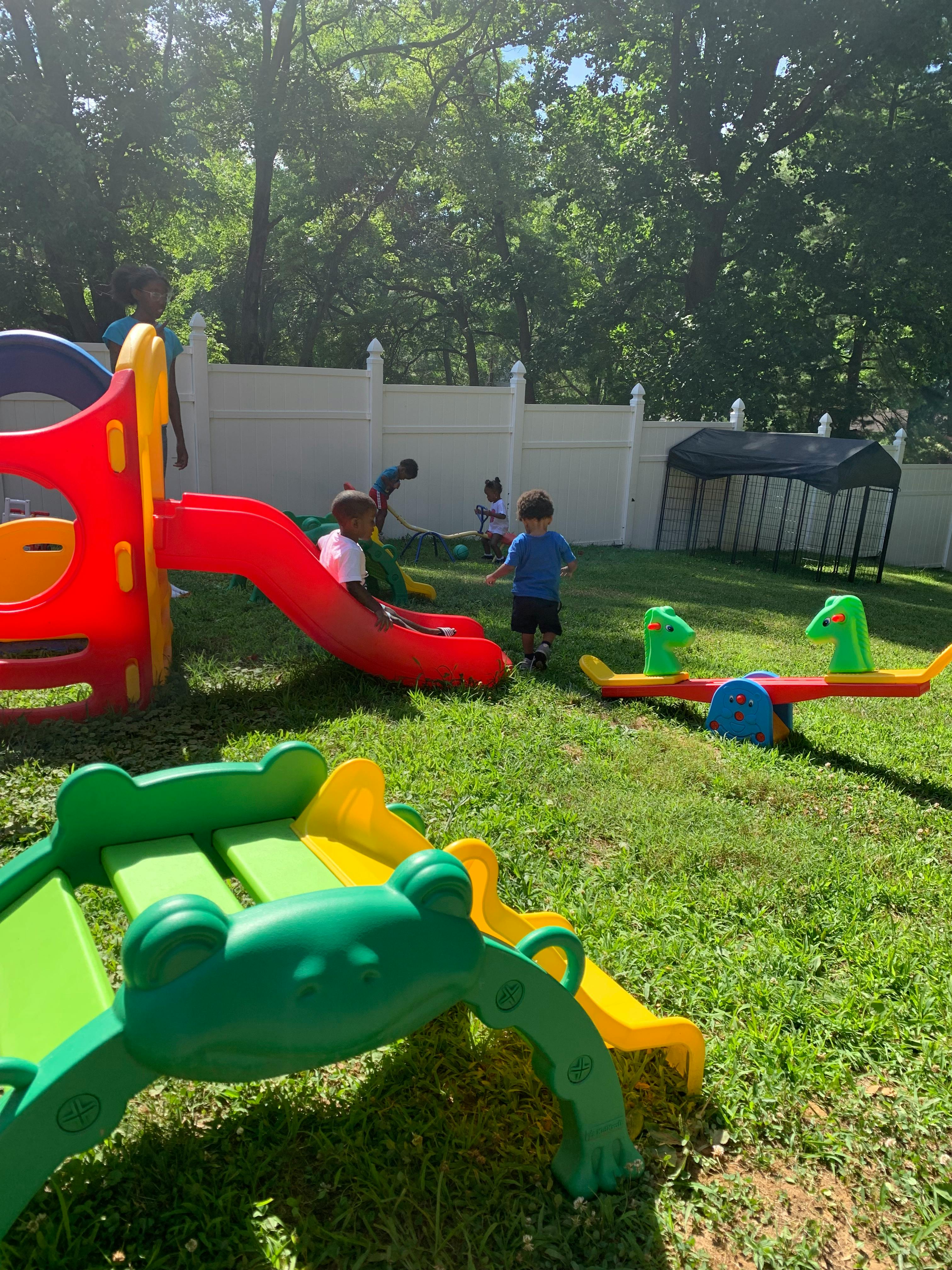 Children playing on a red slide and a green seesaw in a grassy yard