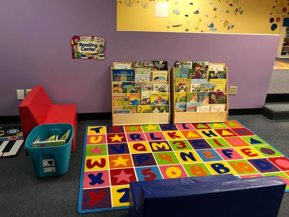 Children's reading corner with book displays, a red chair, and an alphabet rug