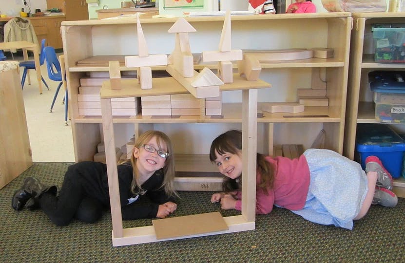 Two children lying on the floor under a wooden block structure