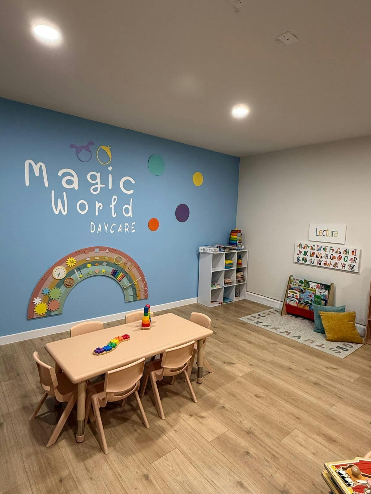 Playroom with a table and chairs, storage shelf, and wall decor that reads "Magic World Daycare"