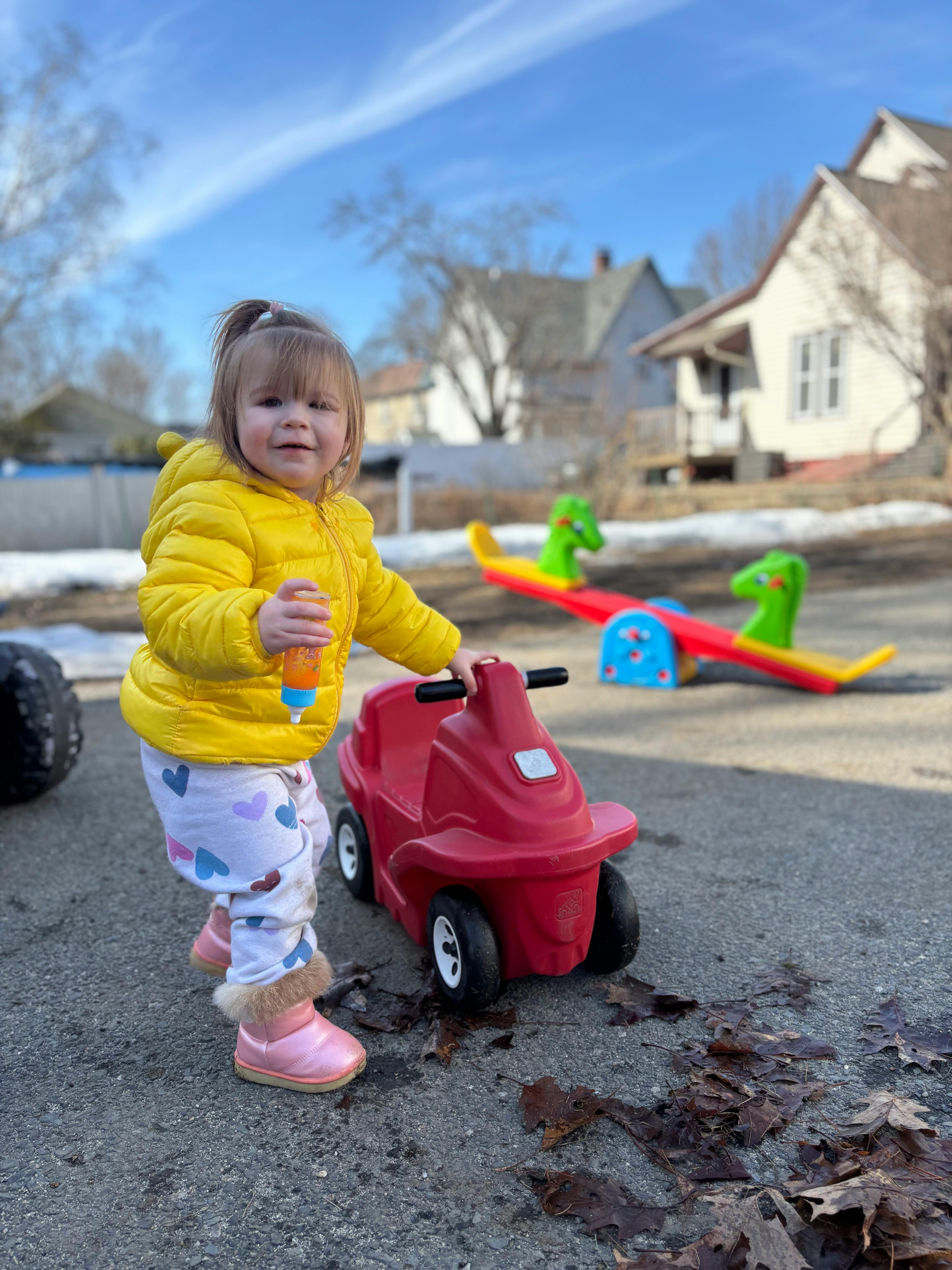 Child in yellow jacket standing next to a red toy car
