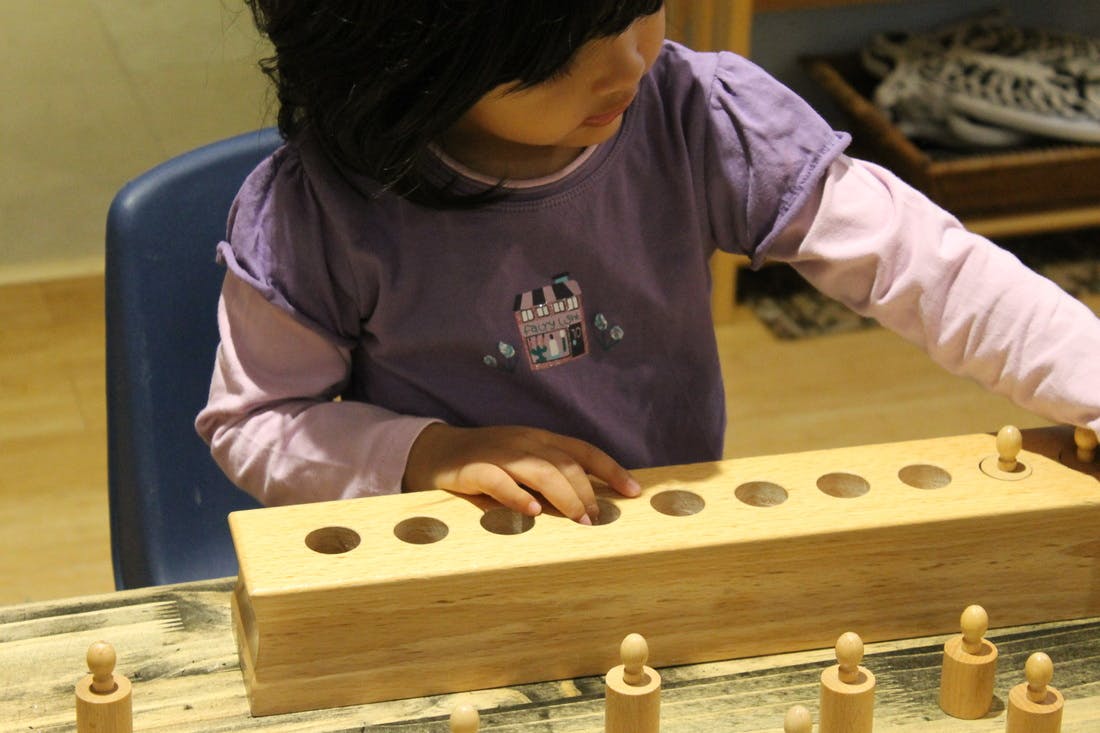 Child playing with a wooden peg and hole toy