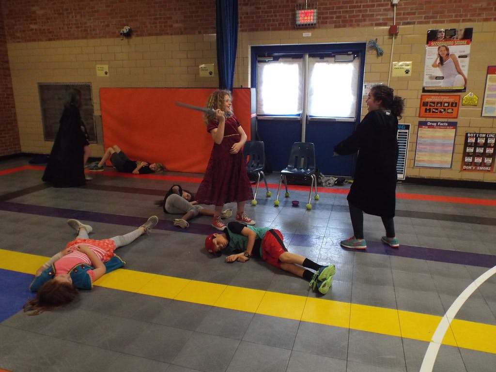 Children playing in a gym, some lying on the floor, one holding a sword
