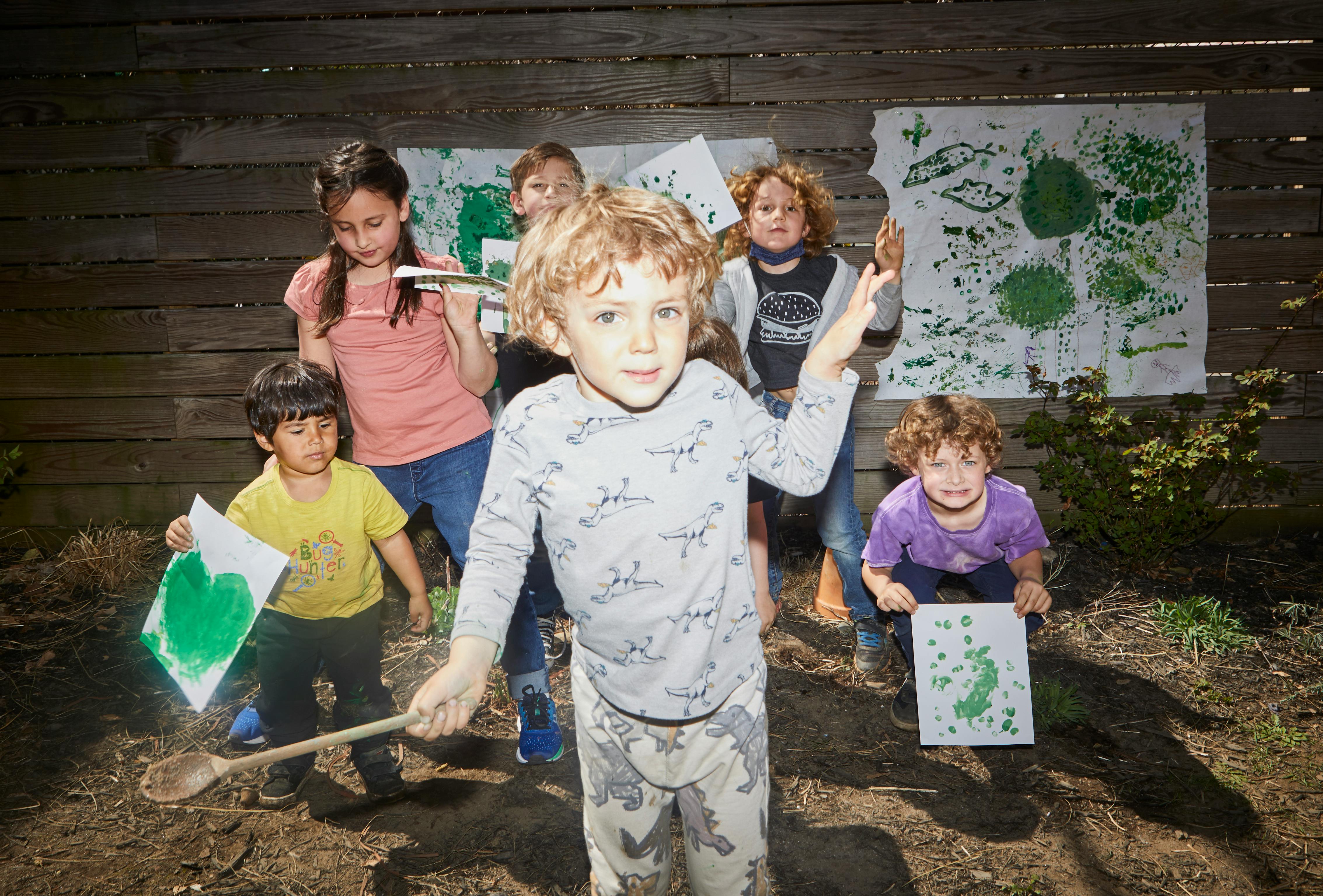 Children holding papers with leaf prints and a wooden spoon