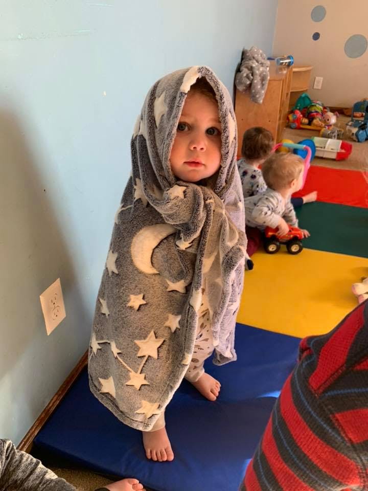 Child wrapped in a blanket with stars and moons, standing on a mat