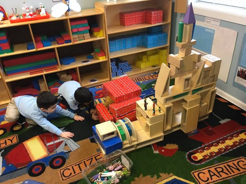 Two children playing with blocks on a colorful rug in a classroom
