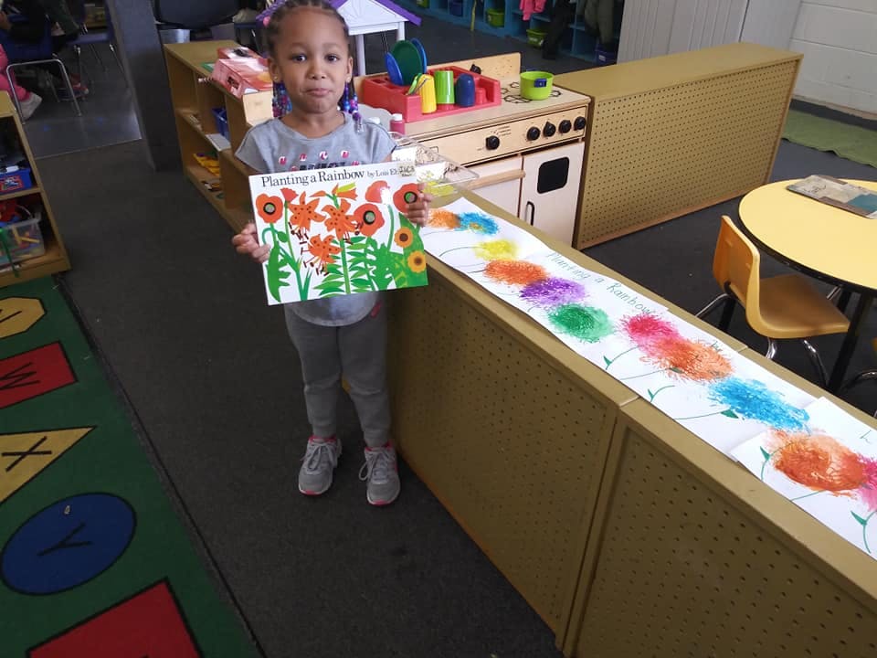 Child holding up a drawing of flowers in a classroom