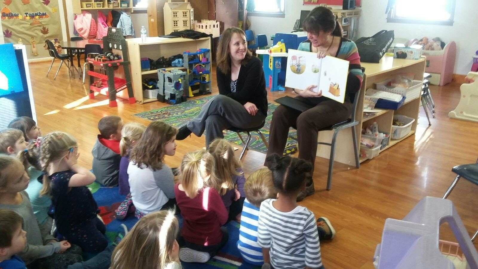 Two people reading a book to a group of children in a classroom