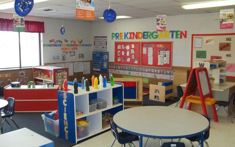 An empty pre-kindergarten classroom with tables, chairs, and learning stations