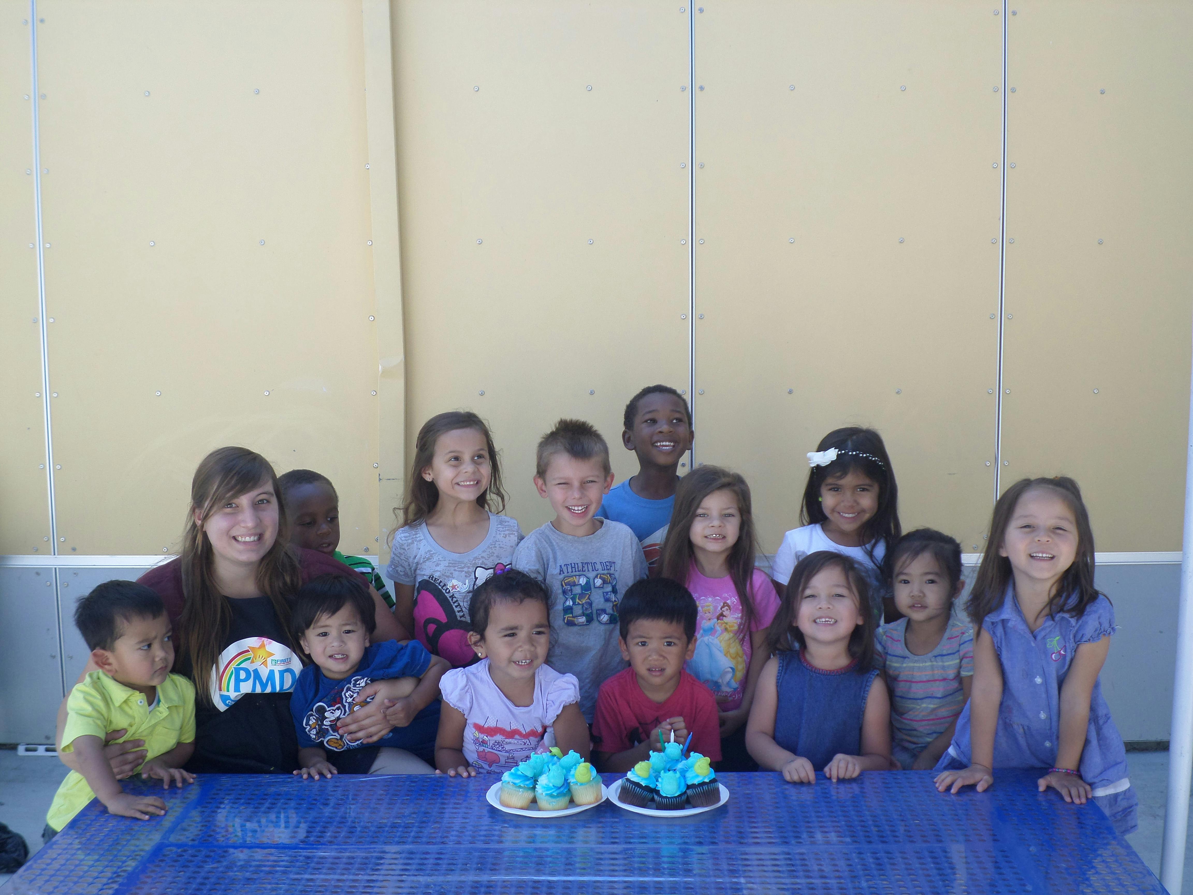 Group of children and one teen posing with cupcakes on a table