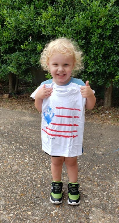 Child holding up a white t-shirt with a blue handprint and red stripes