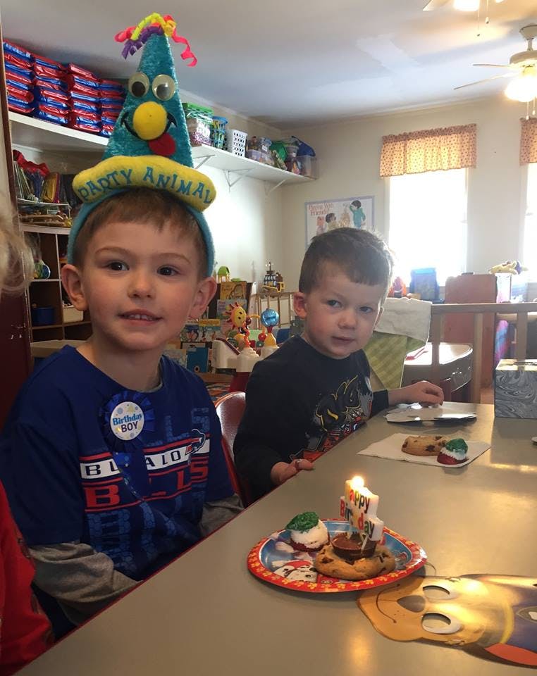 Child wearing a party hat with another child at a table with a lit candle