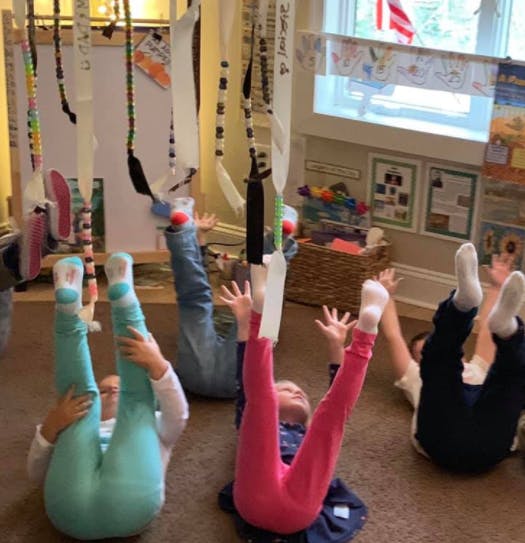 Children lying on their backs with legs raised, interacting with hanging objects