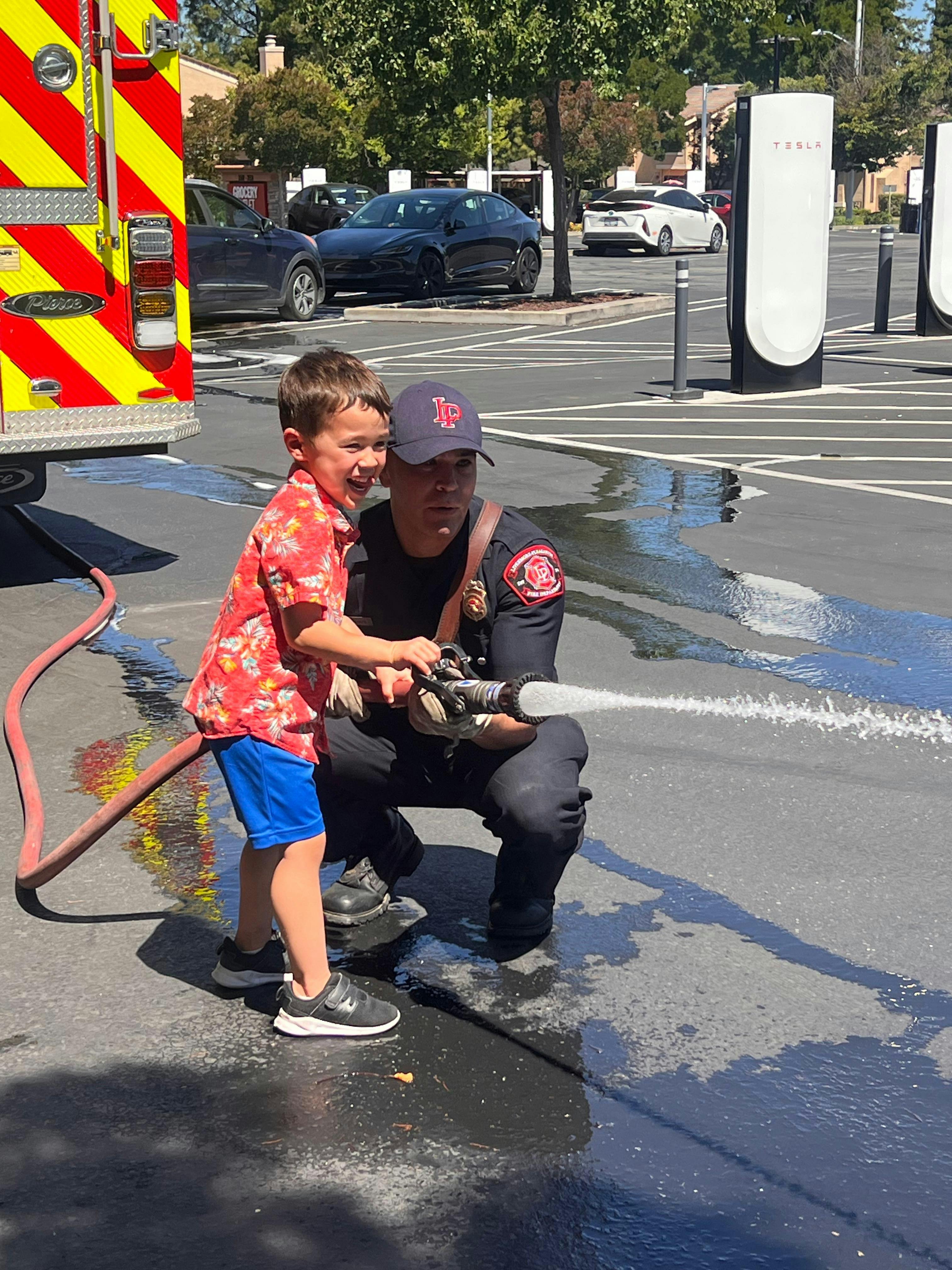 A person in a uniform and a child holding a fire hose spraying water