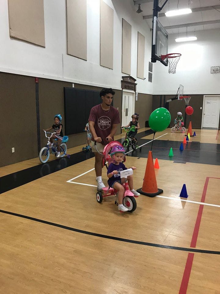 Person helping a child on a pink tricycle in a gymnasium