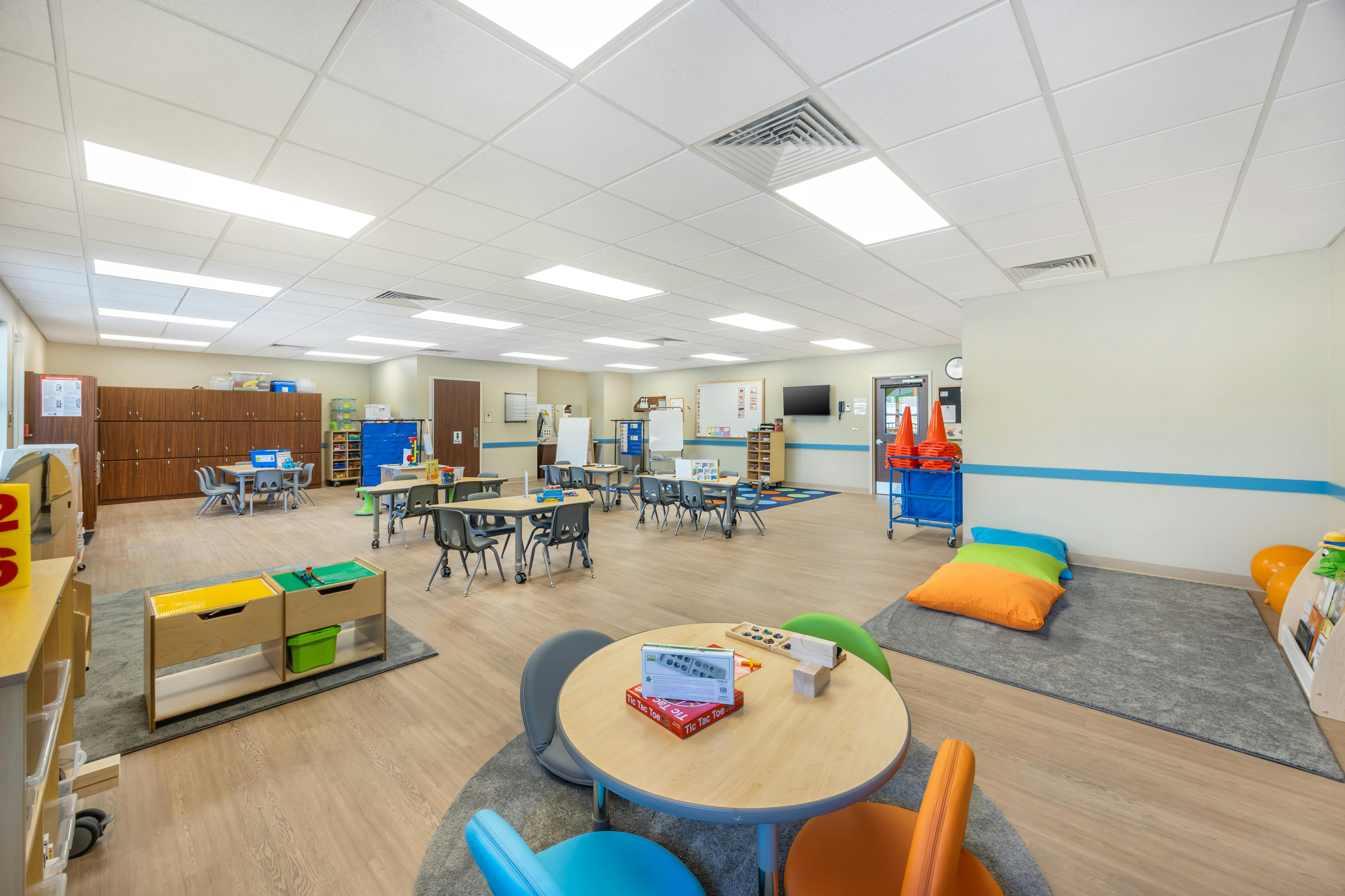 Classroom with small tables and chairs, storage cabinets, and floor cushions