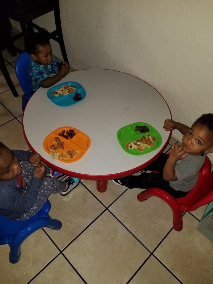 Three children sitting at a round table with plates of food