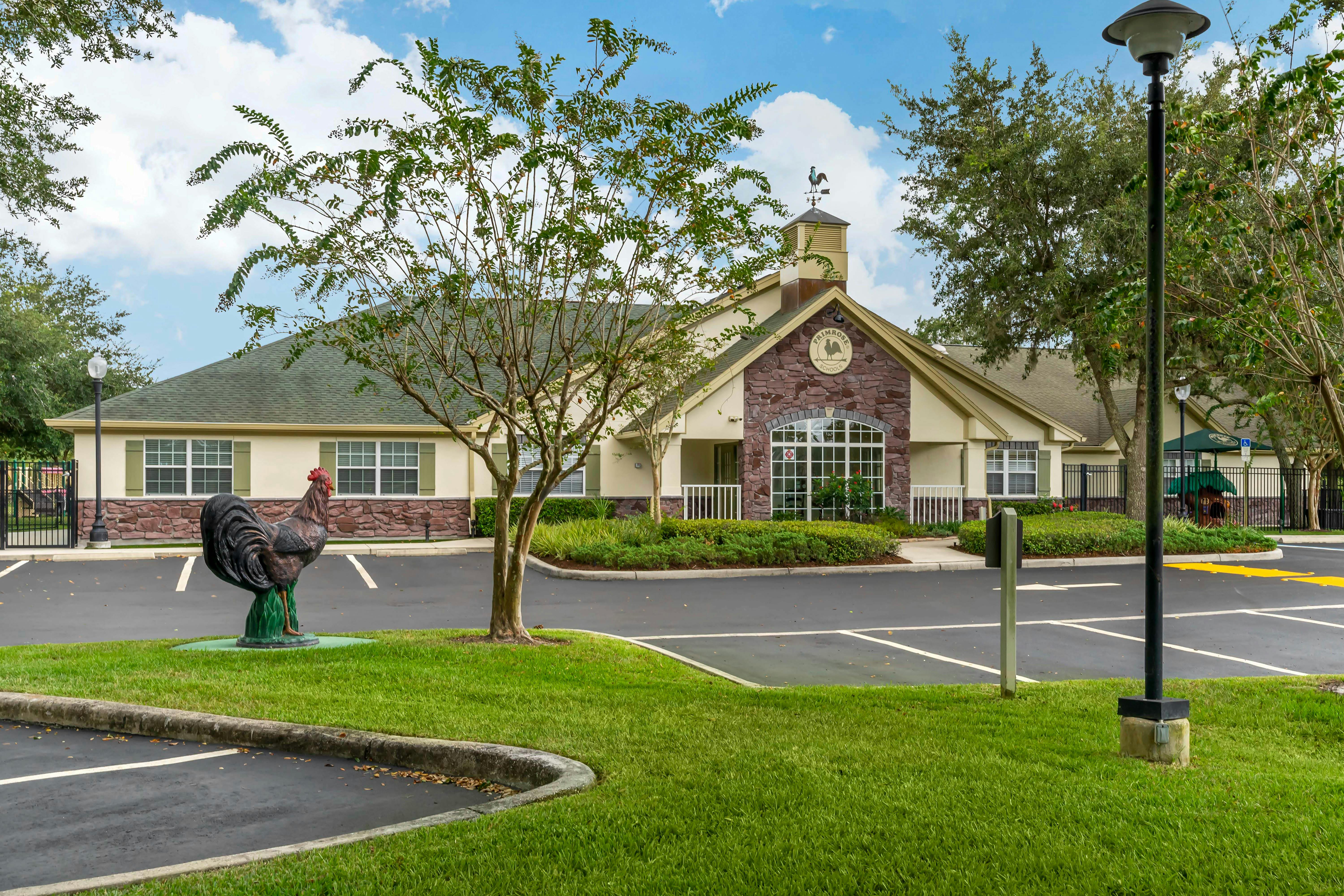 A rooster statue in a parking lot with a building in the background
