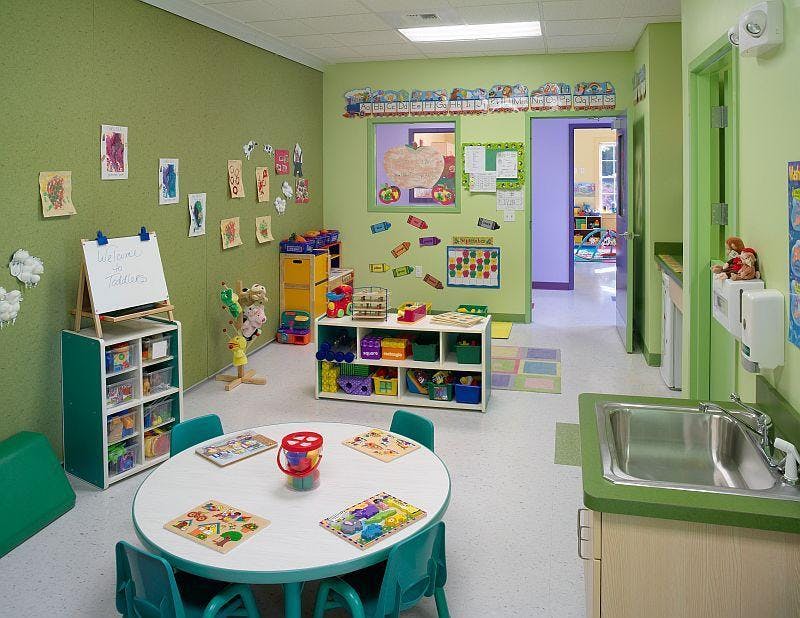 Classroom with small tables and chairs, storage shelves, and a sink