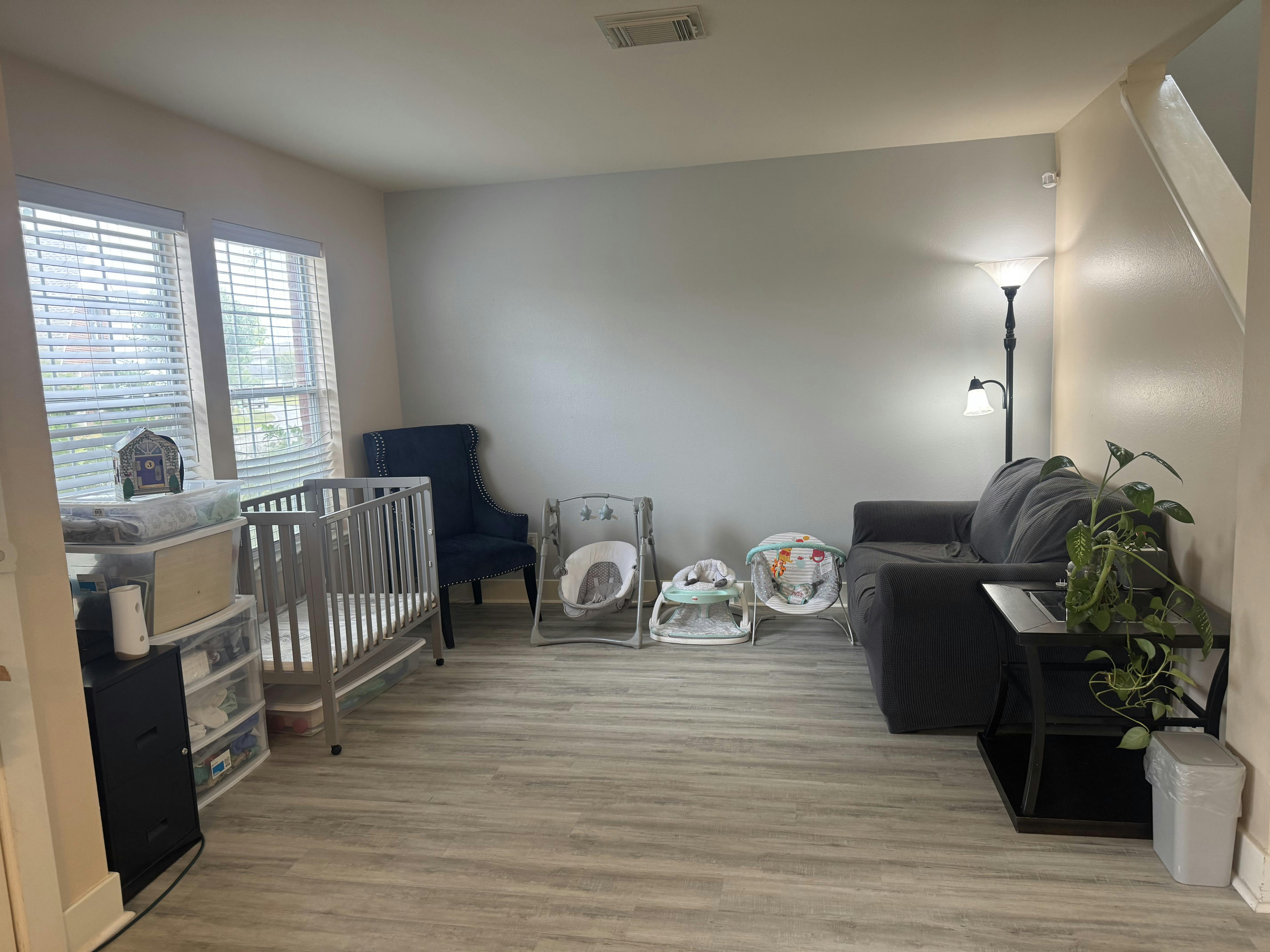 Living room with a crib, baby seats, sofa, and floor lamp