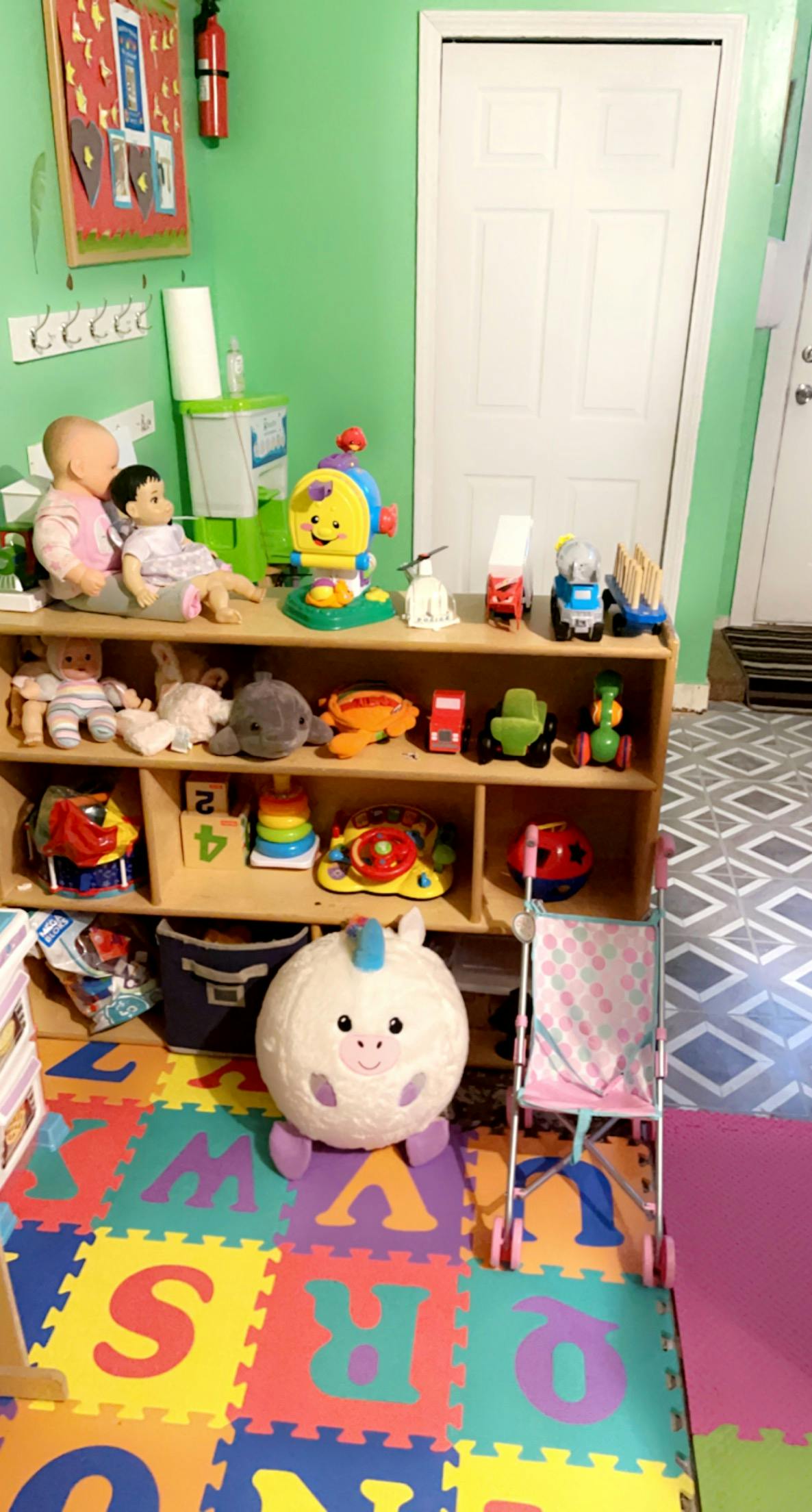 Shelves filled with toys and dolls in a room with alphabet floor mats