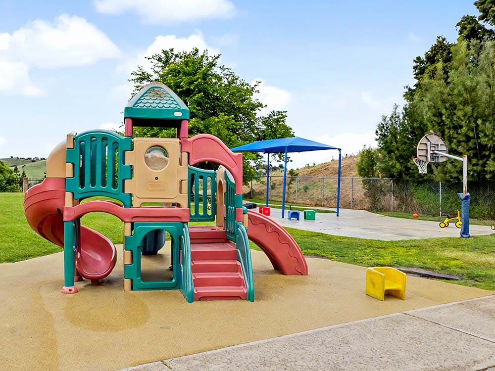 Colorful playground structure with slides and a basketball hoop nearby