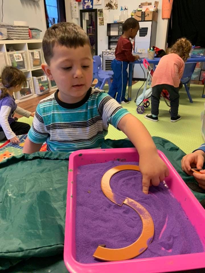 Child tracing letter S in purple sand