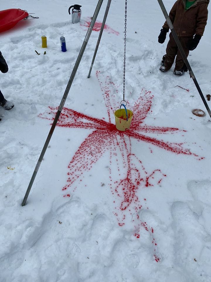 Red liquid dripping from a bucket onto snow, creating a starburst pattern