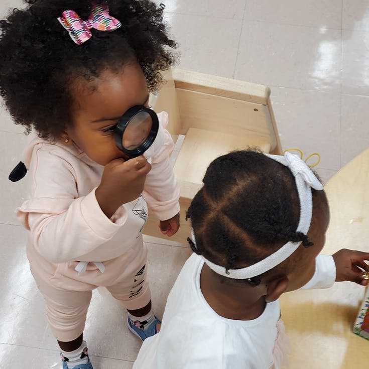 Child looking through a magnifying glass next to another child