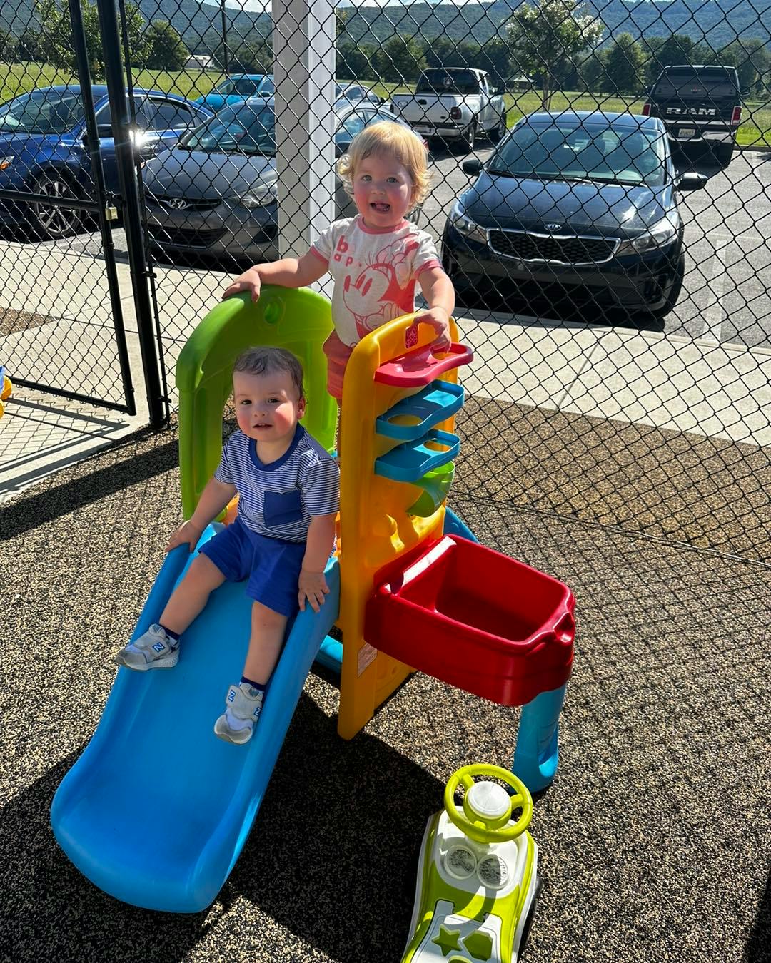 Two children playing on a small slide and play structure outdoors