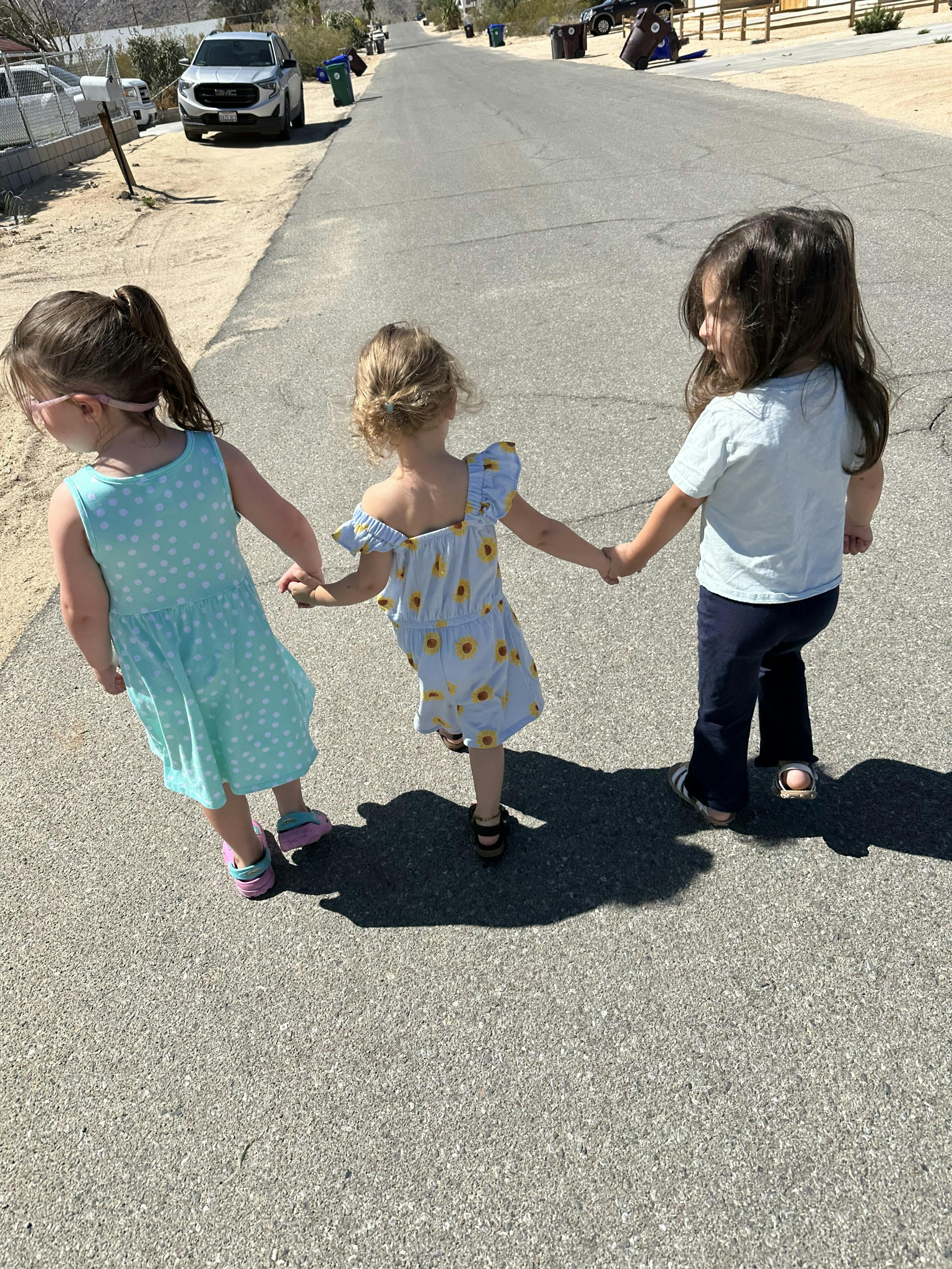 Three children holding hands and walking on a paved road