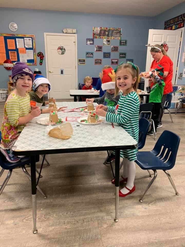 Children and adults decorating gingerbread houses in a classroom