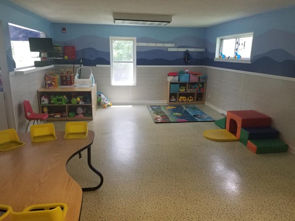 Empty classroom with small tables, chairs, and play equipment