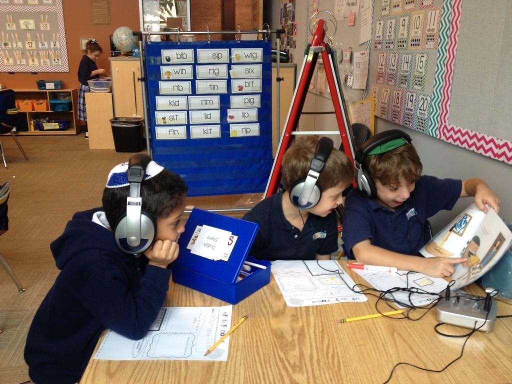 Three children wearing headphones in a classroom