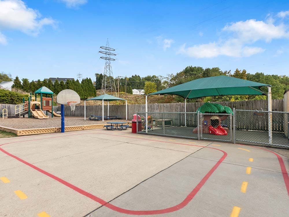 Outdoor playground with slides, swings, basketball hoop, and shaded picnic tables