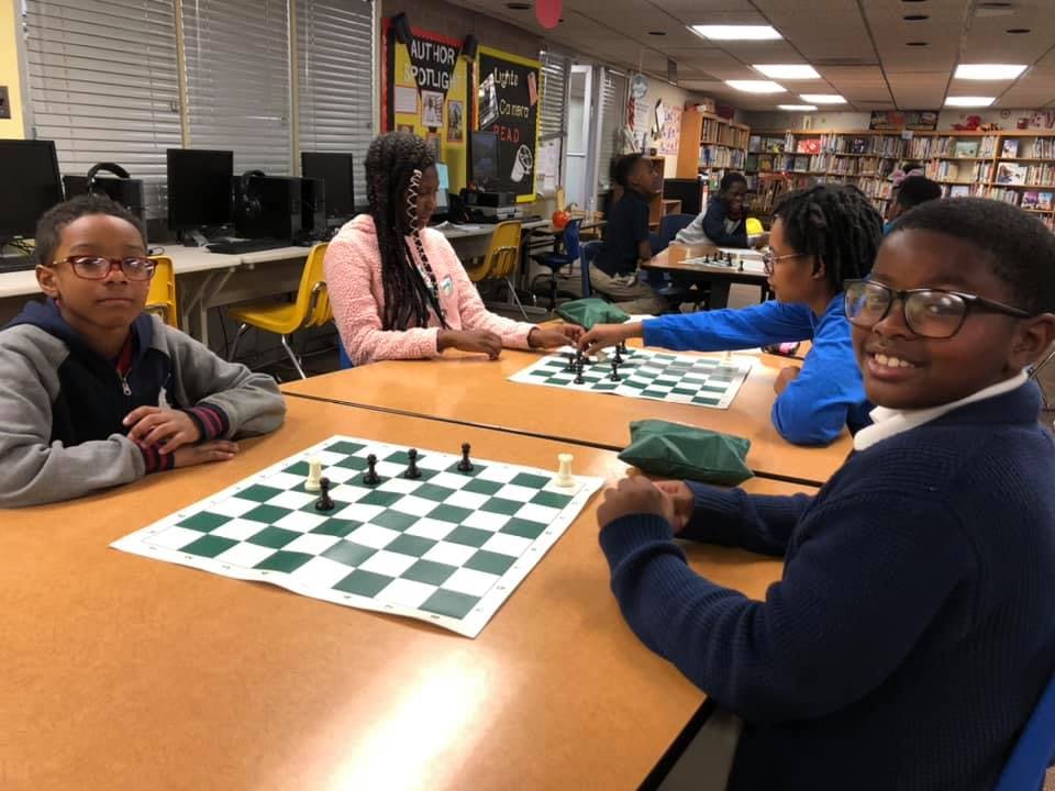 Children playing chess at tables in a room