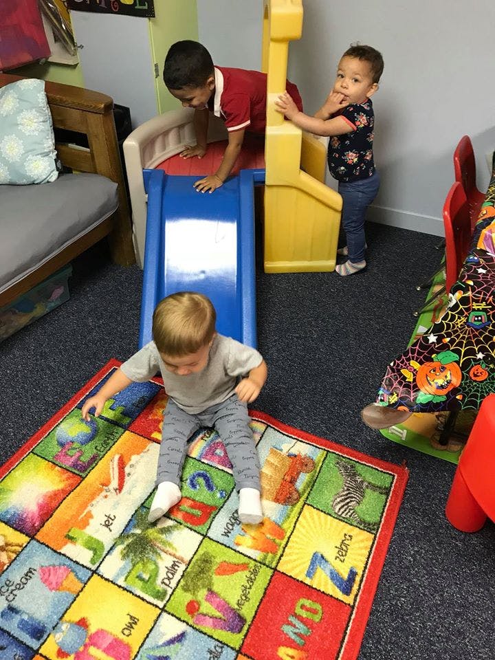Three children playing on a slide and an alphabet rug in a classroom