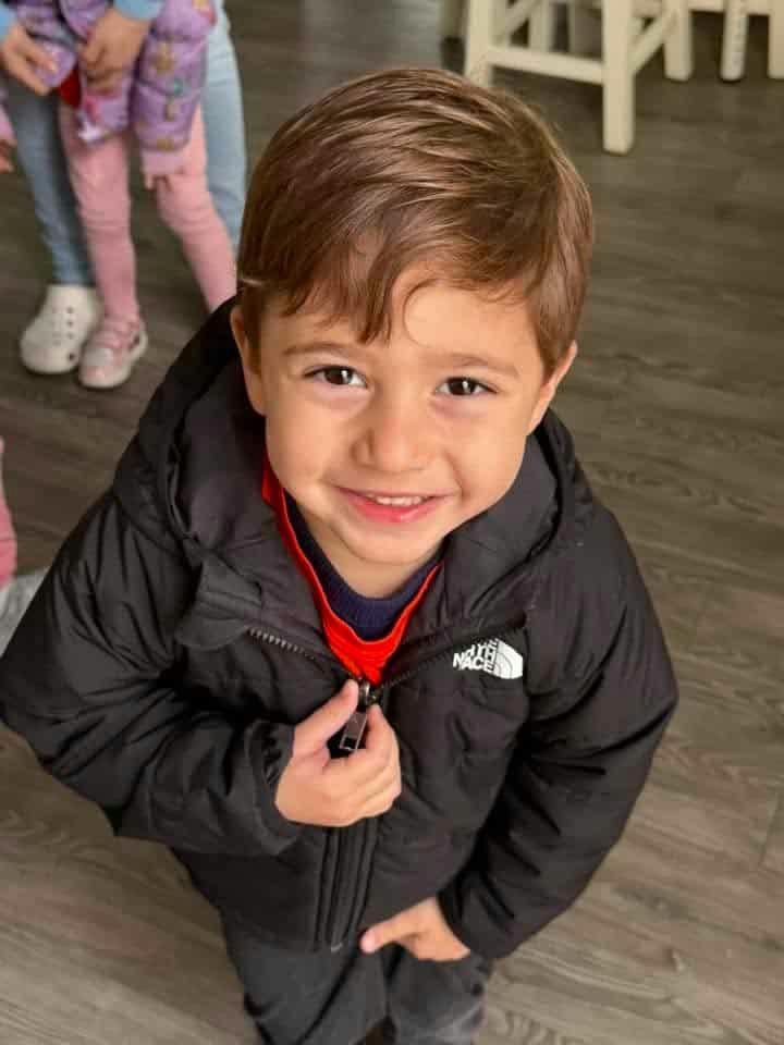 A young child zipping up a black jacket